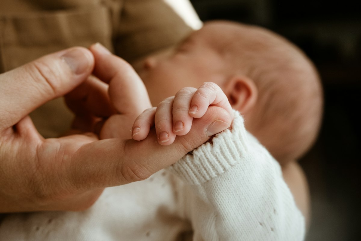 A newborn's hand wrapped around an adult's finger